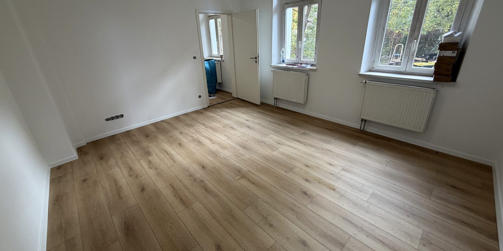 Sanierter Altbauraum mit großen Fenstern und neuem Holzboden